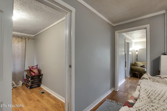 hallway featuring visible vents, a textured ceiling, wood finished floors, and crown molding