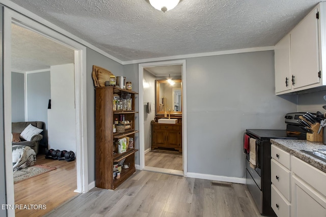 kitchen featuring a textured ceiling, white cabinets, light wood-style flooring, and electric range