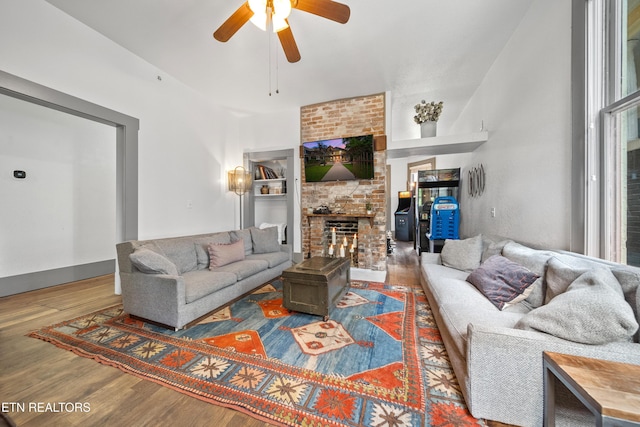 living area featuring wood finished floors, a large fireplace, and a ceiling fan