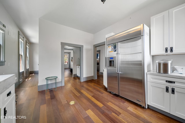 kitchen with built in refrigerator, white cabinets, baseboards, and wood-type flooring