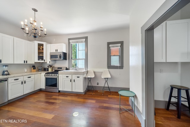 kitchen with dark wood-style flooring, white cabinetry, stainless steel appliances, and an inviting chandelier