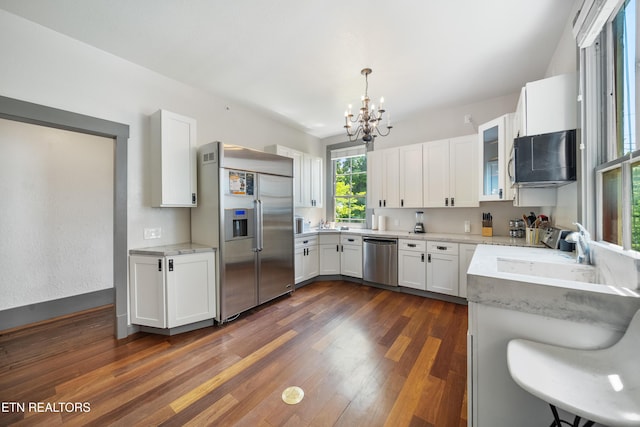 kitchen with white cabinetry, light stone countertops, stainless steel appliances, dark wood-type flooring, and an inviting chandelier