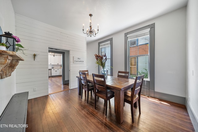 dining room featuring wood walls, a notable chandelier, and dark wood finished floors