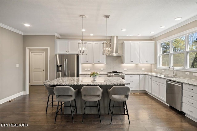 kitchen featuring crown molding, a kitchen island, a sink, appliances with stainless steel finishes, and wall chimney exhaust hood