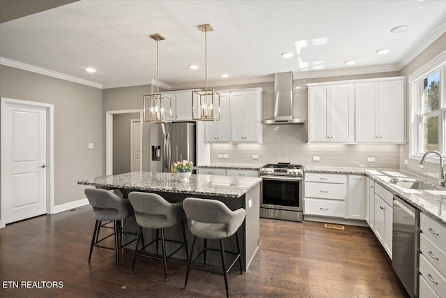 kitchen featuring a sink, wall chimney exhaust hood, a center island, stainless steel appliances, and ornamental molding