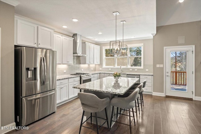 kitchen with tasteful backsplash, stainless steel appliances, a breakfast bar, white cabinets, and wall chimney exhaust hood