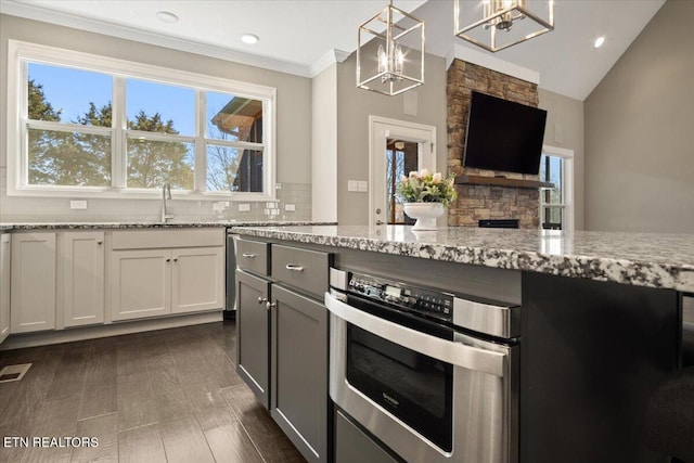 kitchen featuring a chandelier, stainless steel oven, a sink, light stone counters, and backsplash