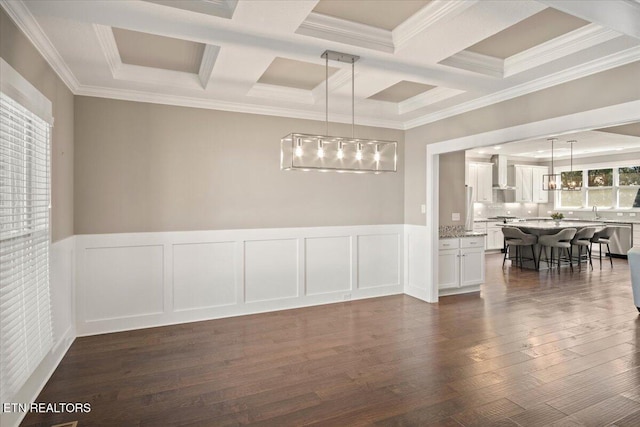 unfurnished dining area with coffered ceiling, dark wood-style flooring, ornamental molding, a wainscoted wall, and beamed ceiling