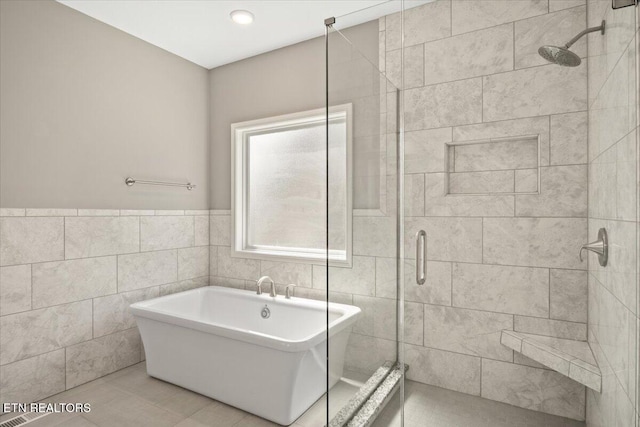 full bath featuring a shower stall, a freestanding bath, tile patterned flooring, and tile walls