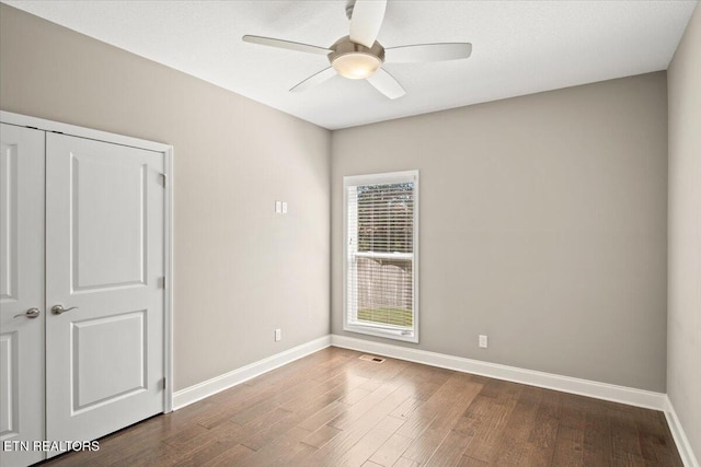 unfurnished room featuring dark wood finished floors, baseboards, visible vents, and a ceiling fan