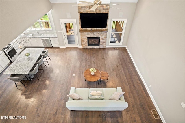 living room featuring dark wood-style flooring, visible vents, baseboards, a fireplace, and ceiling fan