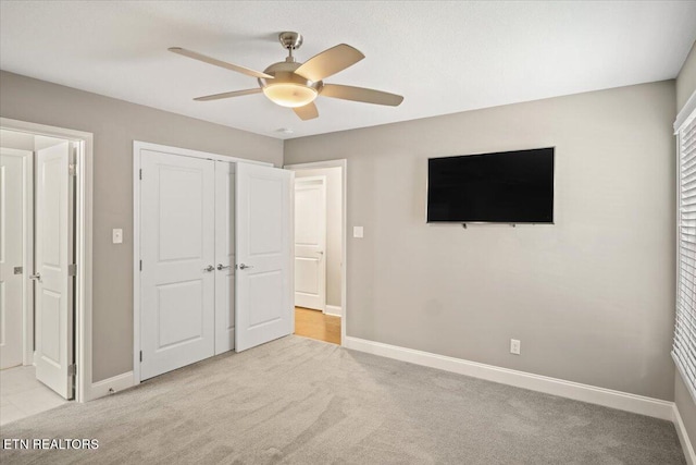 unfurnished bedroom with light carpet, baseboards, a closet, and a ceiling fan