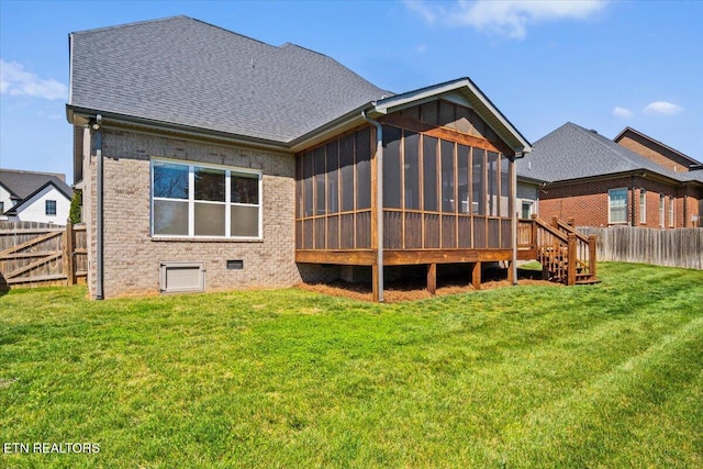 back of property with a fenced backyard, a lawn, a shingled roof, and a sunroom