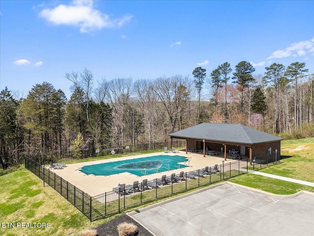 pool featuring a patio, a forest view, fence, and a lawn