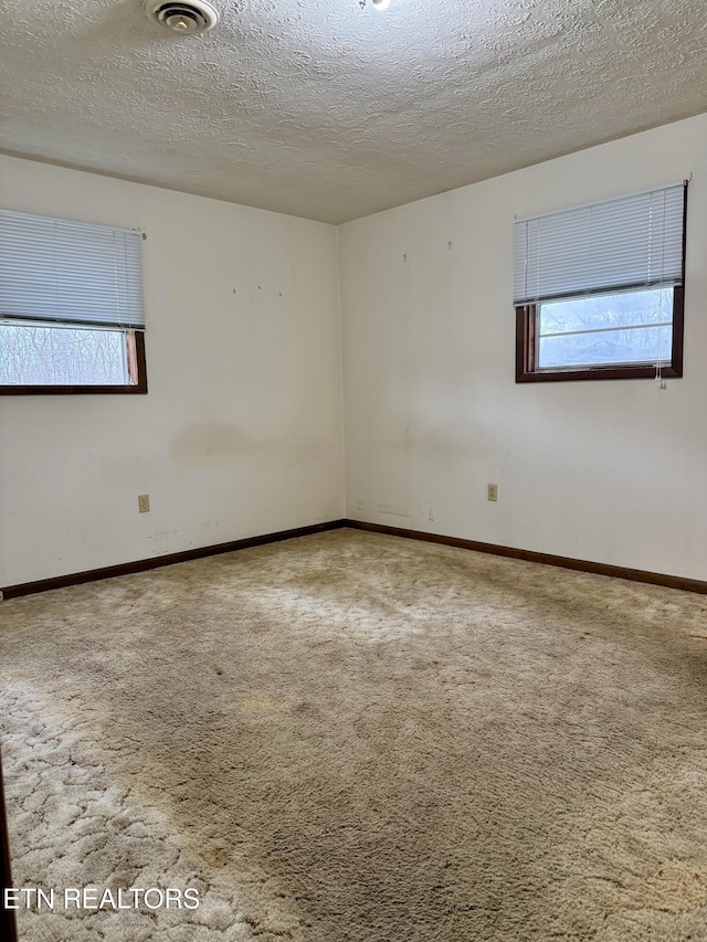 carpeted empty room with baseboards, a textured ceiling, and visible vents