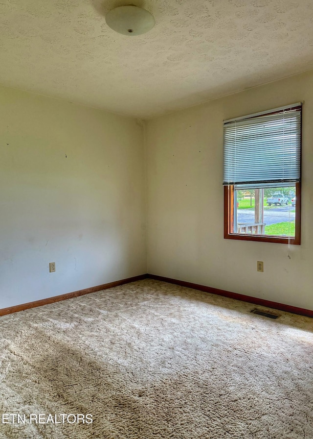 carpeted empty room featuring baseboards, a textured ceiling, and visible vents