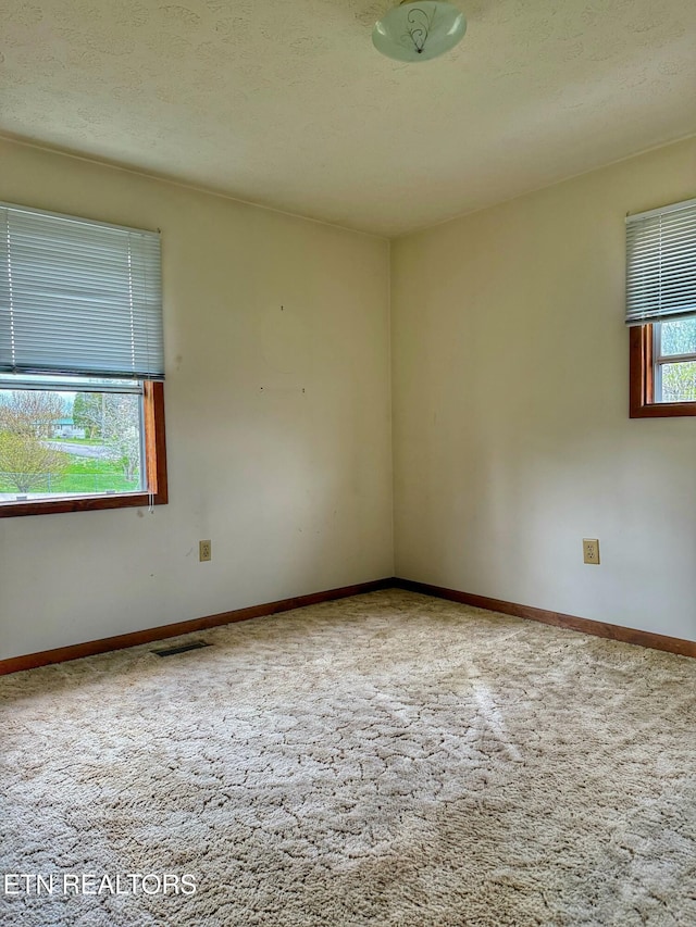 empty room featuring baseboards, visible vents, carpet flooring, and a textured ceiling