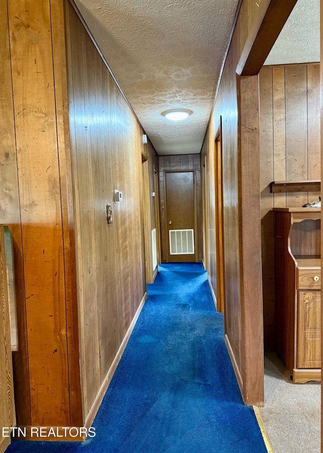 hall with carpet floors, a textured ceiling, visible vents, and wooden walls
