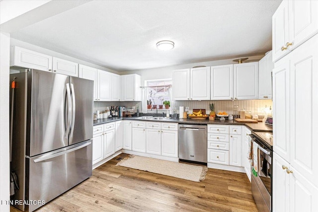kitchen with dark countertops, a sink, white cabinetry, and stainless steel appliances