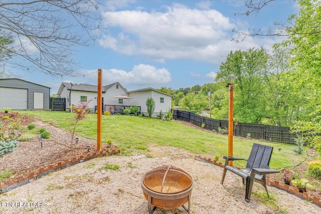 view of yard with a garage, an outdoor fire pit, a fenced backyard, and an outbuilding