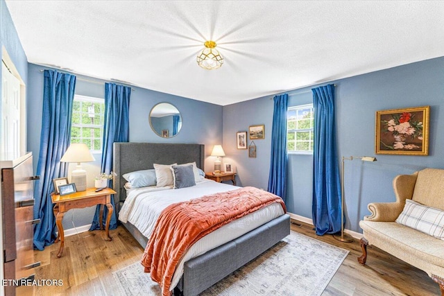 bedroom with multiple windows, wood finished floors, and baseboards