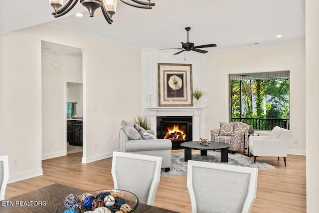 living area with baseboards, light wood-type flooring, ornamental molding, and a warm lit fireplace