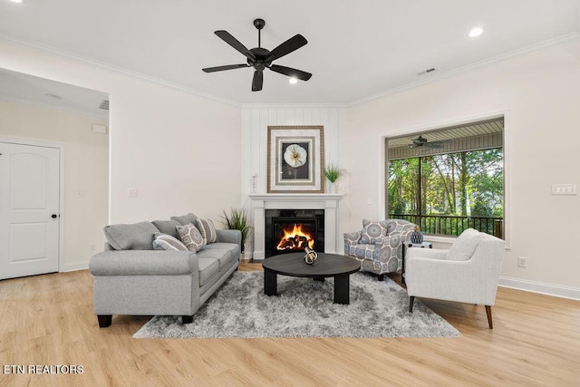 living room with a glass covered fireplace, a ceiling fan, baseboards, ornamental molding, and wood finished floors