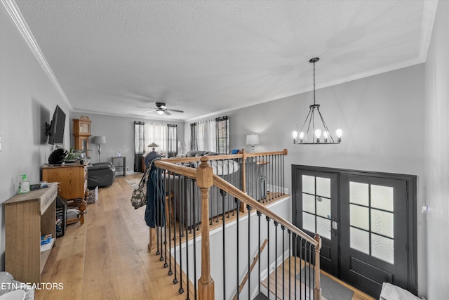 stairway featuring ceiling fan with notable chandelier, a textured ceiling, ornamental molding, and wood-type flooring