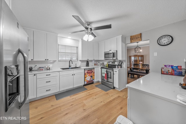 kitchen with stainless steel appliances, a ceiling fan, a sink, light wood-style floors, and white cabinetry