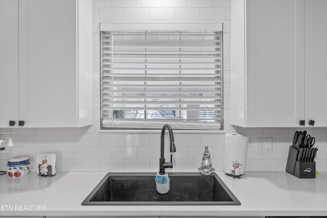 kitchen with decorative backsplash, white cabinetry, a sink, and light countertops