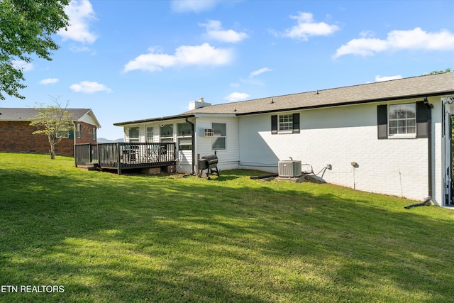 rear view of property with a chimney, central AC unit, a yard, brick siding, and a deck