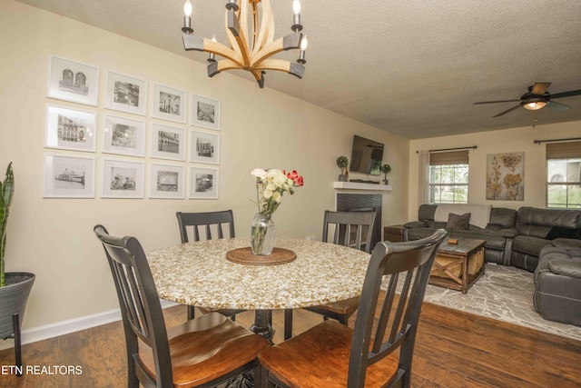 5836 Windtree Ln, Knoxville, TN 37921 - dining area with baseboards, a fireplace, a textured ceiling, dark wood finished floors, and ceiling fan with notable chandelier