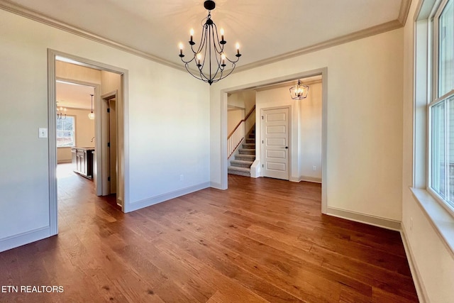 unfurnished dining area featuring stairway, a chandelier, wood finished floors, baseboards, and ornamental molding