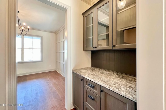 kitchen with glass insert cabinets, light stone counters, wood finished floors, and an inviting chandelier
