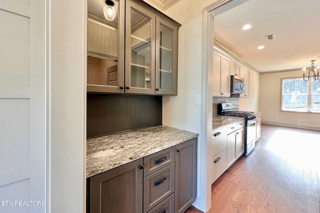 kitchen featuring backsplash, visible vents, appliances with stainless steel finishes, glass insert cabinets, and wood finished floors