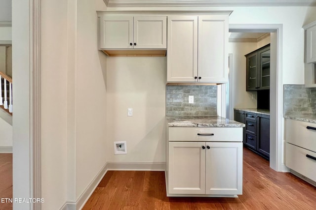 kitchen with backsplash, light stone countertops, wood finished floors, baseboards, and ornamental molding