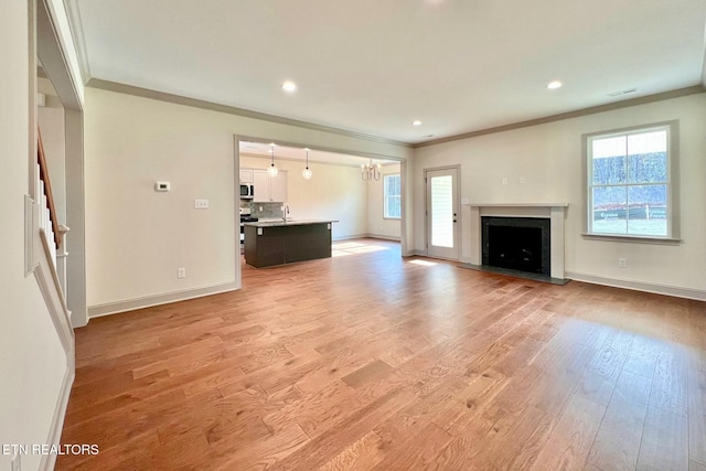 unfurnished living room with plenty of natural light, crown molding, and light wood-style flooring