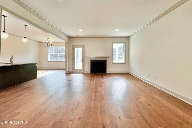 unfurnished living room with a notable chandelier, a sink, a fireplace with flush hearth, baseboards, and light wood-style floors