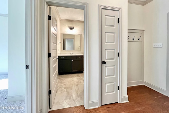 hallway with baseboards, light wood-type flooring, ornamental molding, and a sink