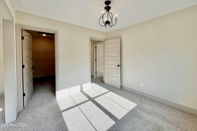 unfurnished bedroom with a closet, carpet floors, a chandelier, a spacious closet, and baseboards