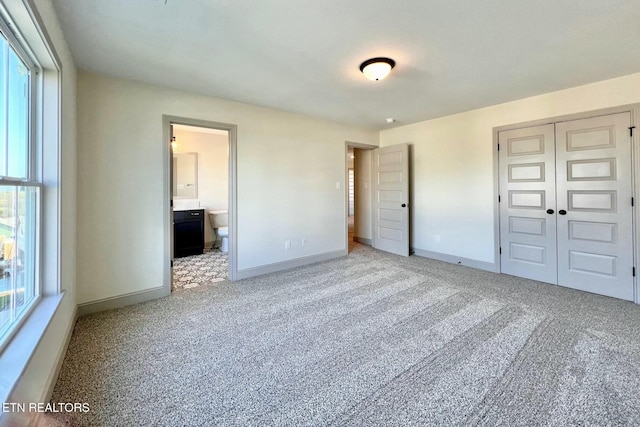 unfurnished bedroom with light carpet, baseboards, a closet, and connected bathroom