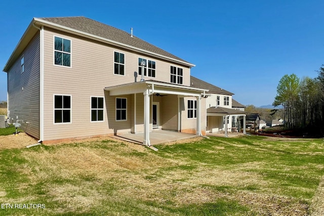 rear view of house with a shingled roof, a patio area, and a yard