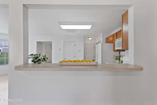 kitchen with brown cabinetry, a peninsula, light countertops, and white appliances
