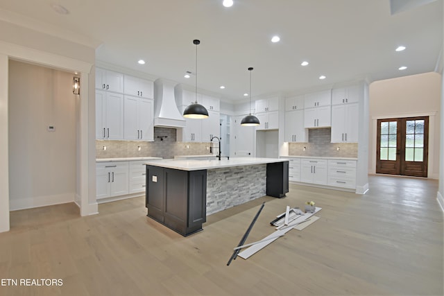 kitchen featuring premium range hood, light wood-style floors, decorative backsplash, a large island, and white cabinetry