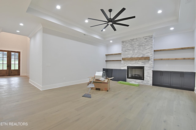 unfurnished living room with a tray ceiling, light wood finished floors, a ceiling fan, baseboards, and crown molding