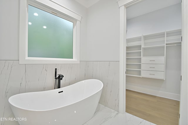 bathroom with a freestanding tub, wainscoting, and a spacious closet