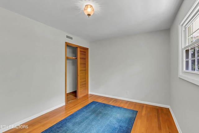 unfurnished bedroom featuring baseboards, wood finished floors, visible vents, and a closet