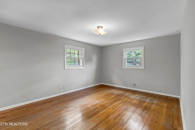 empty room with hardwood / wood-style floors, a wealth of natural light, and baseboards