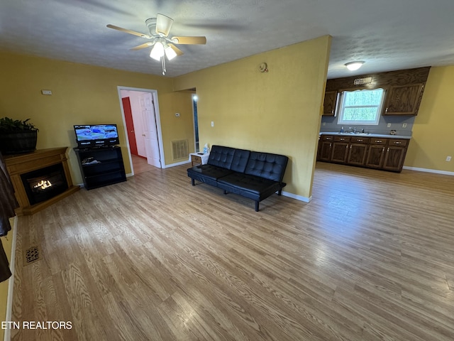 sitting room featuring a ceiling fan, baseboards, light wood finished floors, visible vents, and a warm lit fireplace