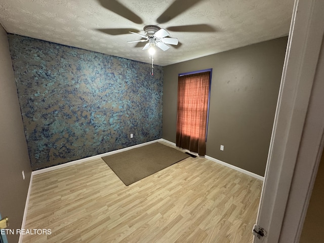 unfurnished room with a textured ceiling, baseboards, light wood finished floors, and ceiling fan